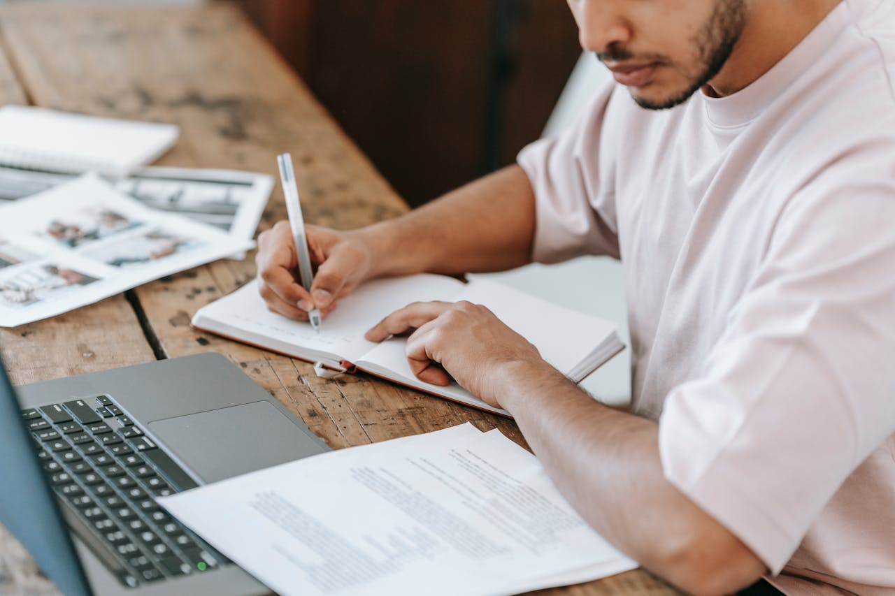 Photo by Michael Burrows: https://www.pexels.com/photo/crop-student-writing-in-agenda-at-desk-with-laptop-7129007/